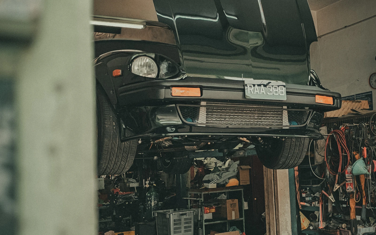 A classic car raised on a lift with its hood up in a working garage bay