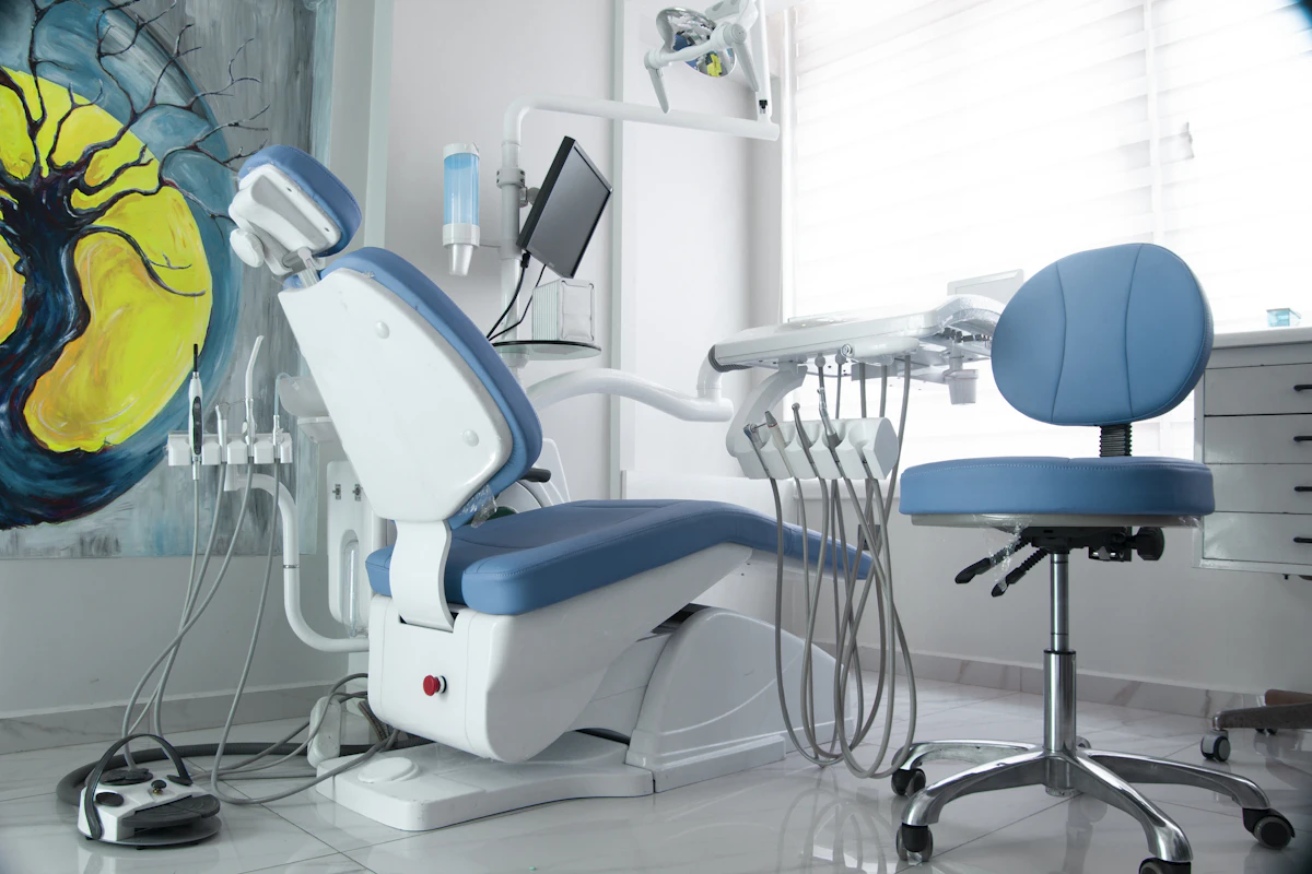 A modern dental operatory with a blue treatment chair, delivery unit and art on the wall