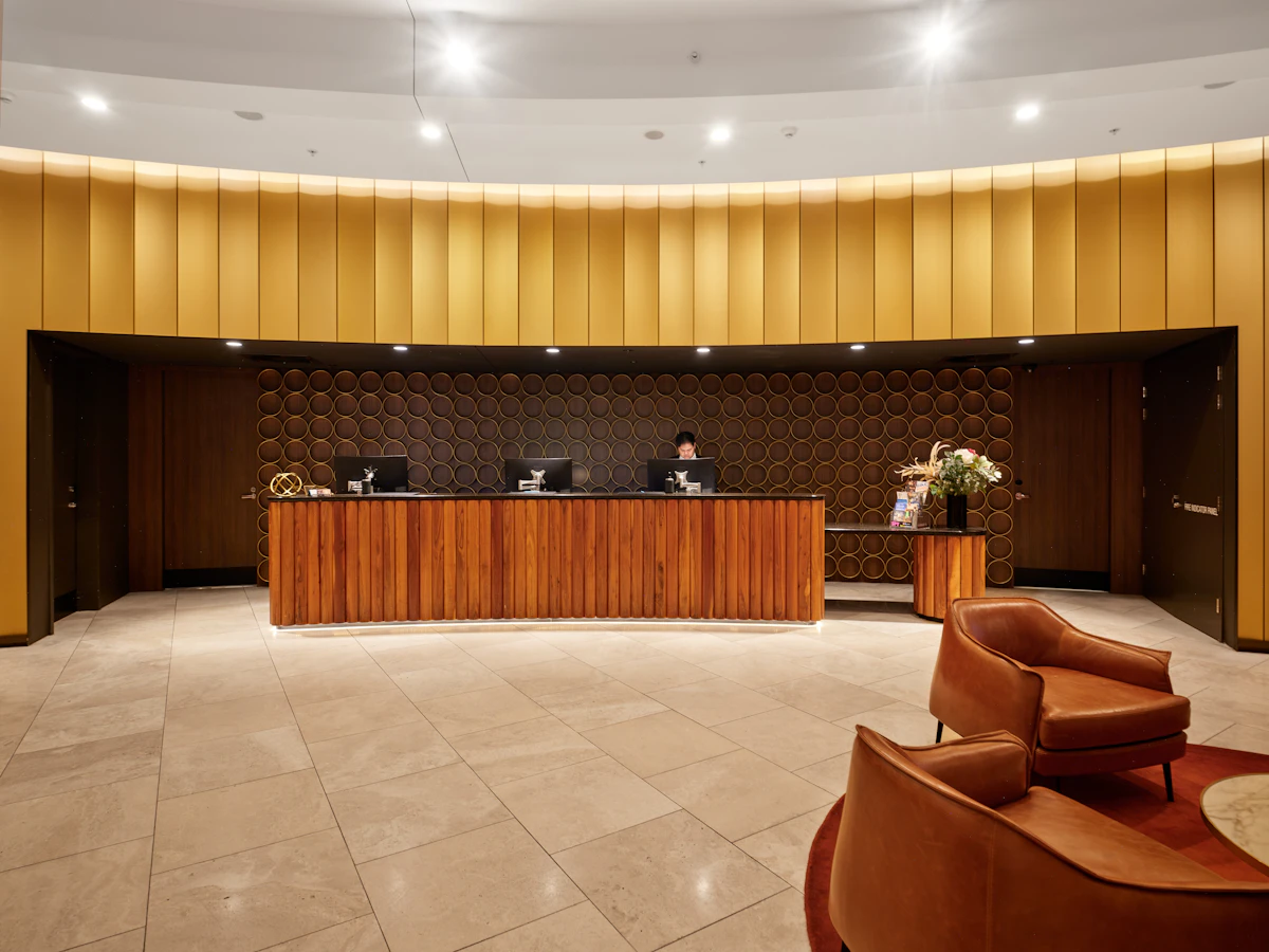 A staffed hotel reception desk in warm wood, lounge chairs in the foreground