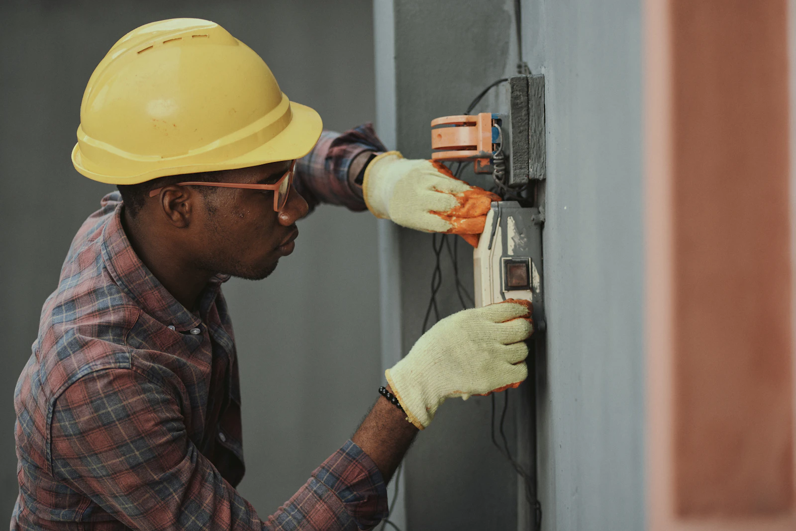 A gloved technician in a hard hat servicing a wall-mounted control unit