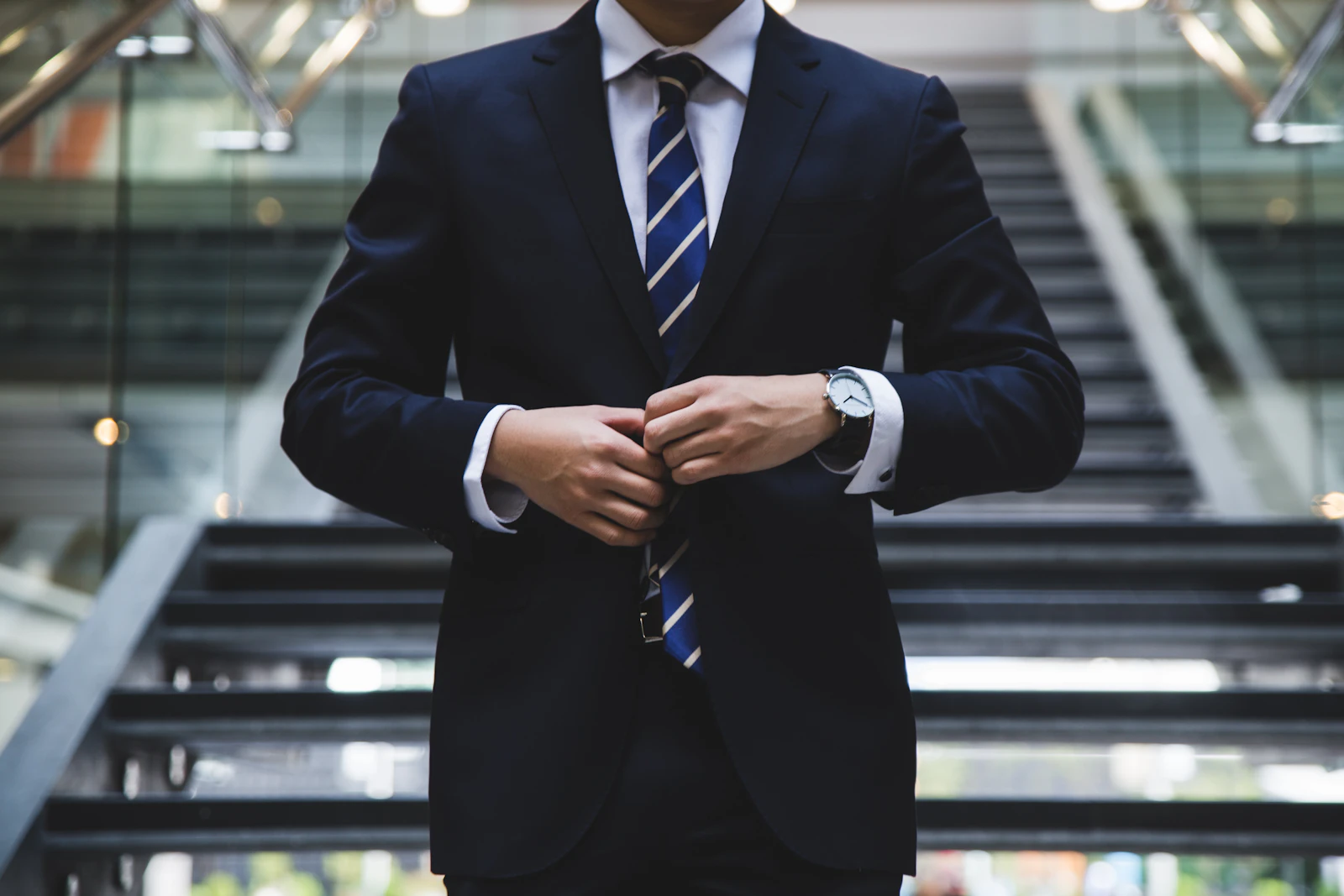 An attorney in a tailored navy suit buttoning his jacket at the foot of an office staircase