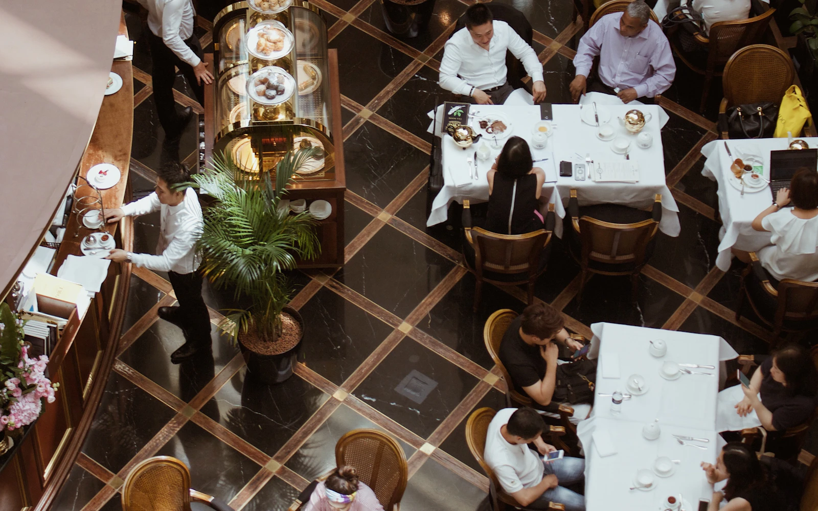 A full dining room mid-service seen from above — white tablecloths, servers moving between tables