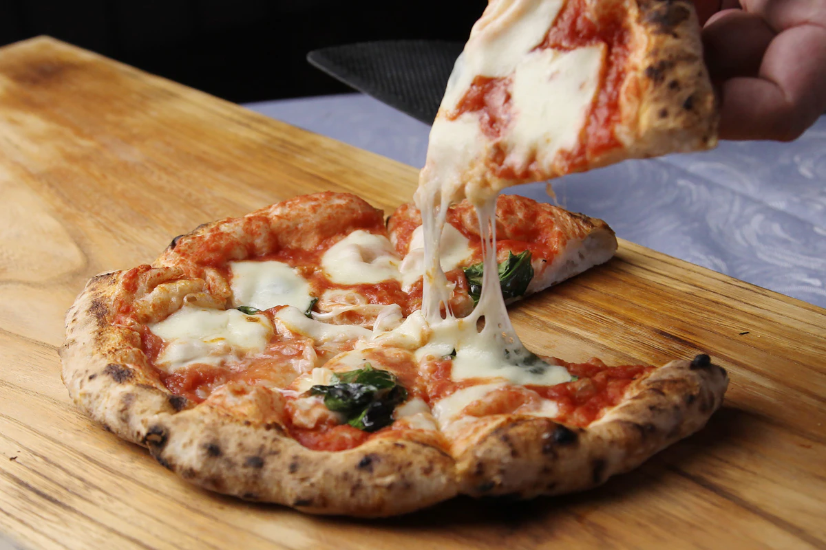 A slice being lifted from a fresh wood-fired pizza on a serving board